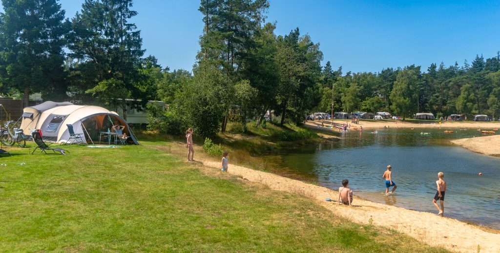 Een hoek van een campingstrand met een tent en kinderen die spelen in het zand en het water.